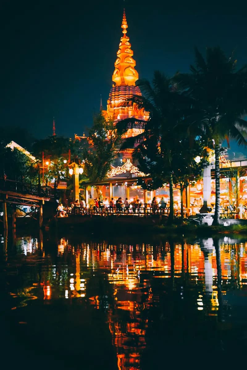 Golden Dai pagoda at night with palms and water reflections in Xishuangbanna