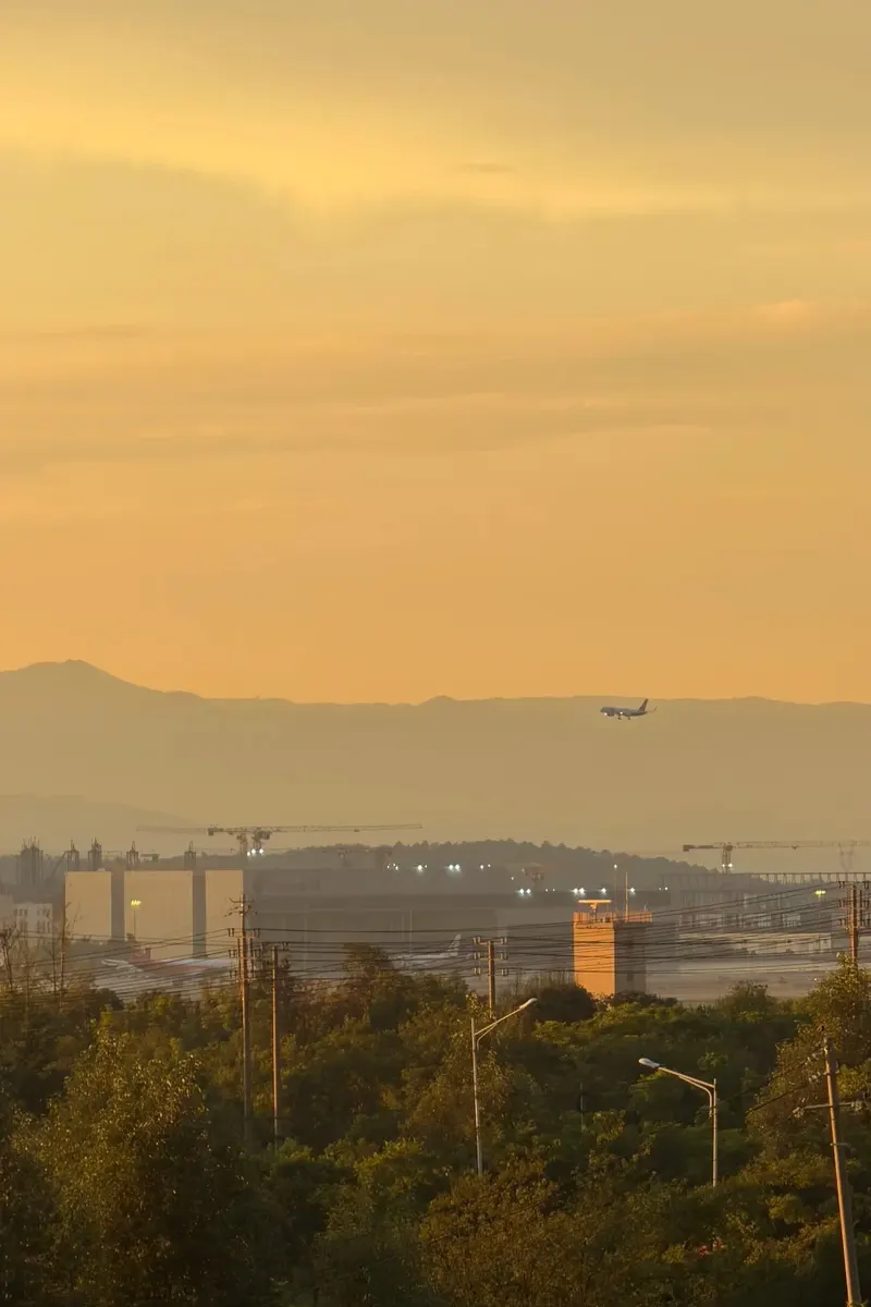 Plane lifting off past mountains at golden hour, Kunming airport