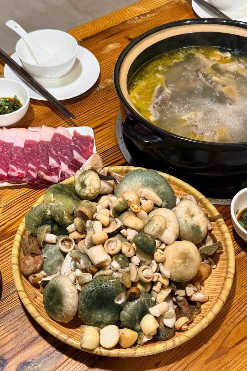 Basket of wild mushrooms beside a simmering chicken-broth hotpot, Yunnan
