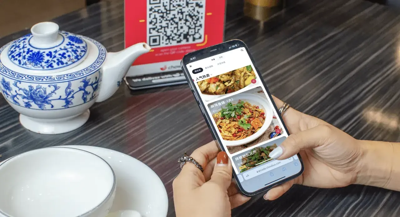 Person scanning QR code at Chinese restaurant table to browse food menu on phone