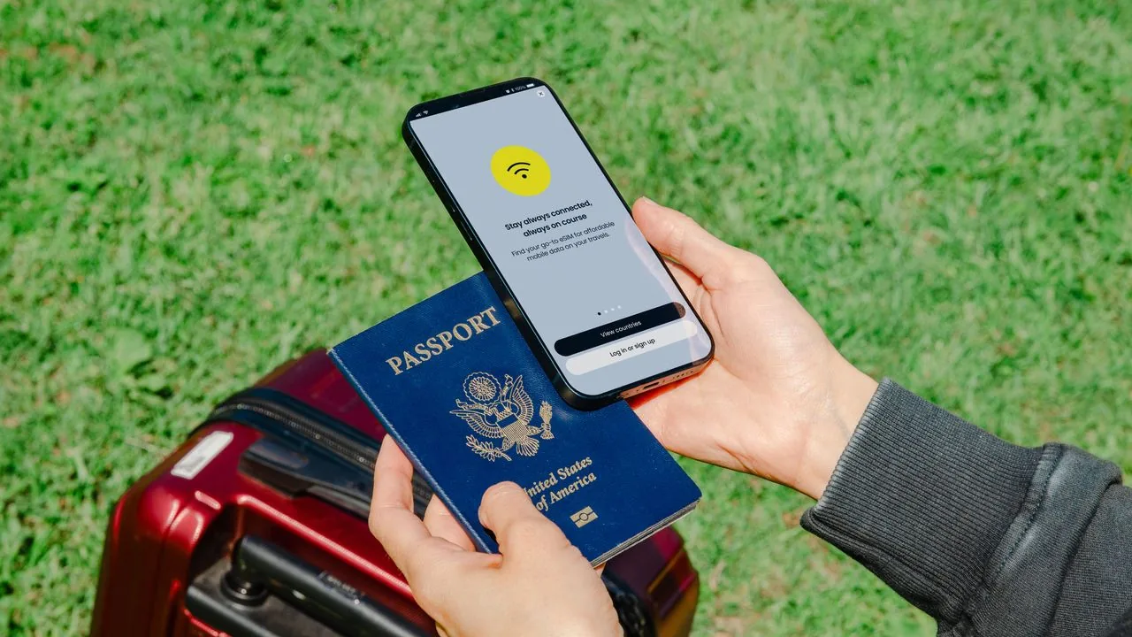 Traveler holding a phone and passport beside luggage while preparing an eSIM before departure