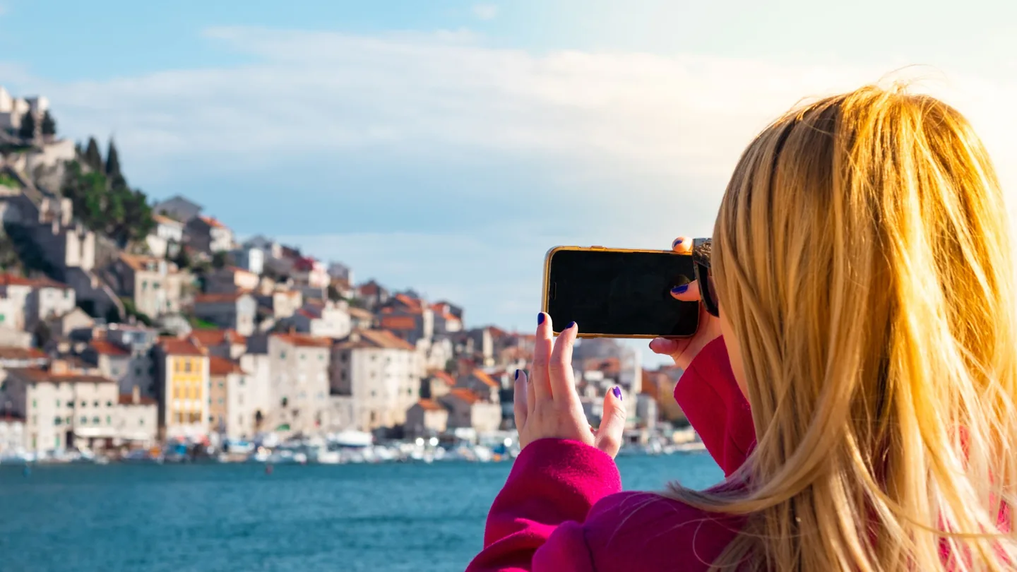 Traveler using a smartphone by the waterfront; illustrative photo about mobile connectivity while traveling