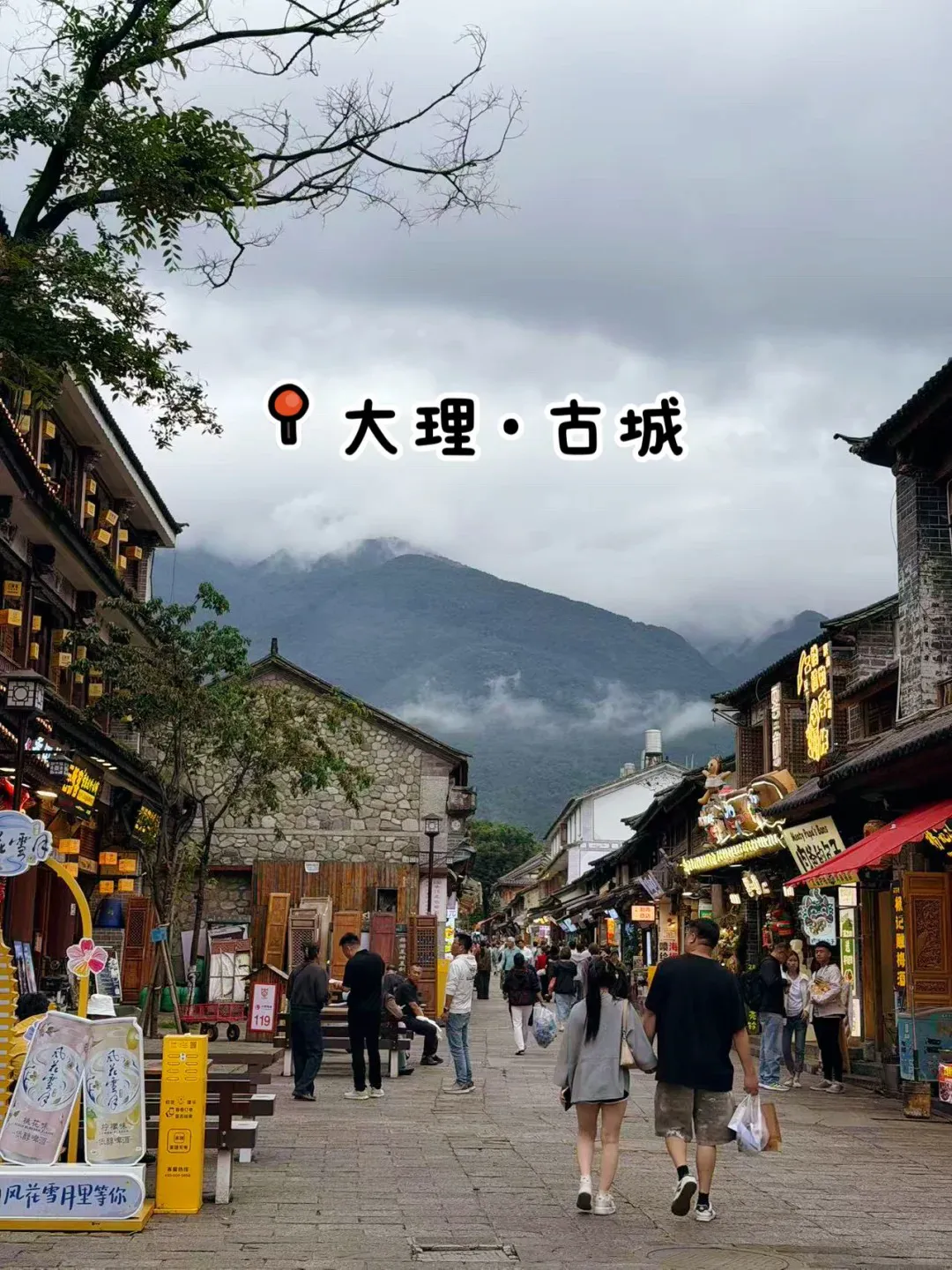 Pedestrian street in Dali Ancient Town with shops, visitors, and Cangshan in cloud
